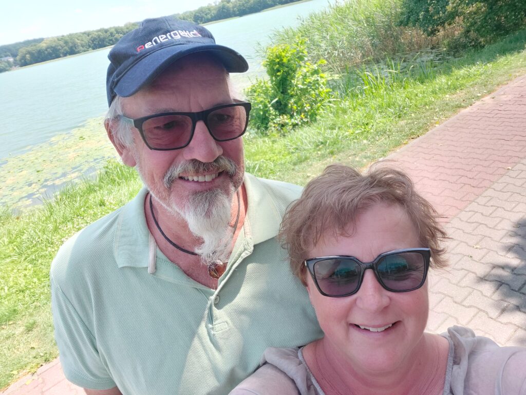 Martina und Günter Görlach spazieren an einem See entlang, umgeben von Sommergrün.