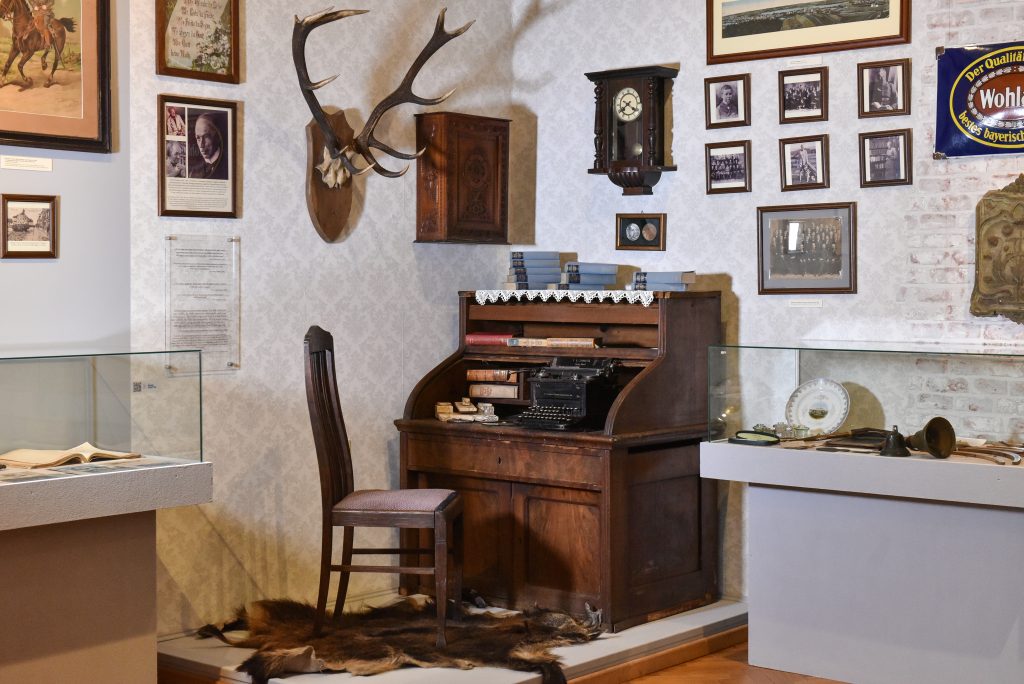 Innenraum des Museums in Mrągowo mit historischem Schreibtisch, Fotografien und regionalen Erinnerungsstücken